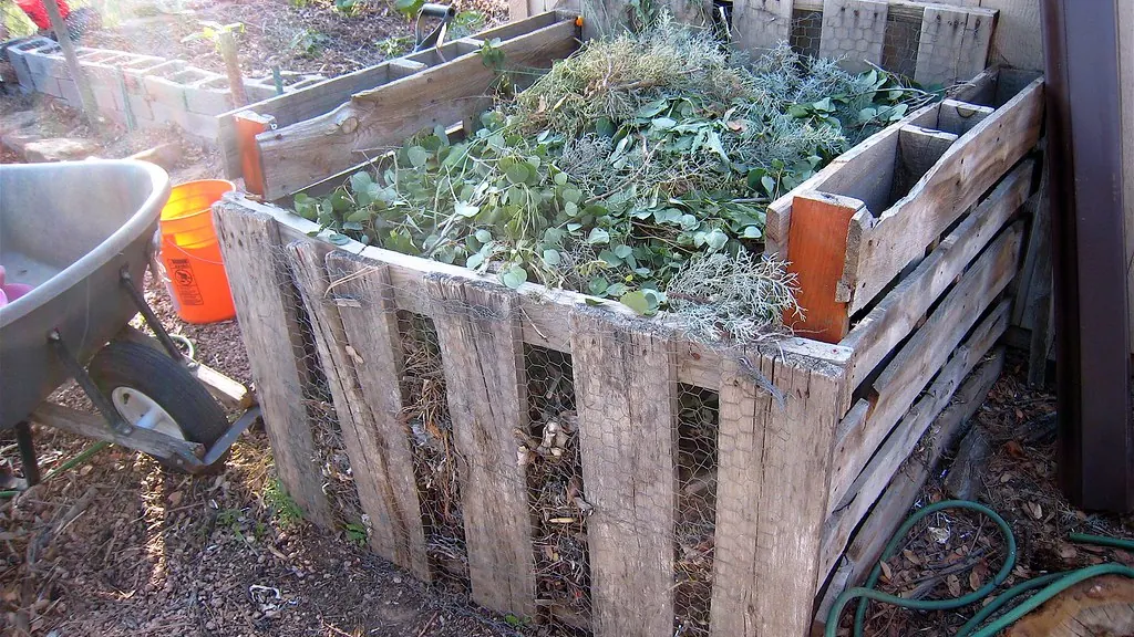 Wooden pallet compost bin filled with garden waste beside a vegetable garden