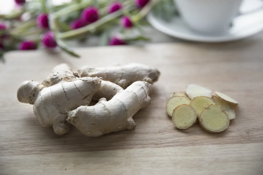 Whole ginger root and fresh slices on a wooden cutting board